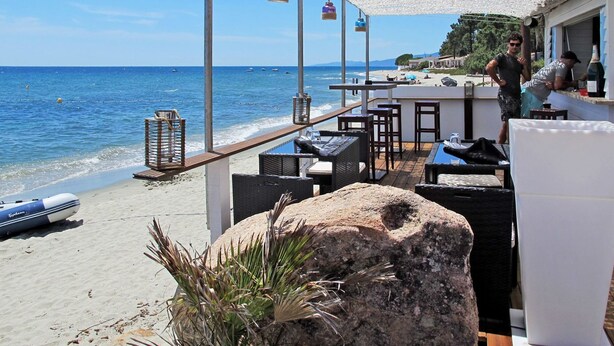 A beachside restaurant with outdoor seating, a view of the sea, and a bar area.