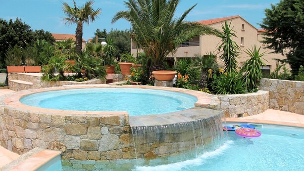 Une piscine circulaire bordée de pierres, entourée de plantes en pot et de palmiers.