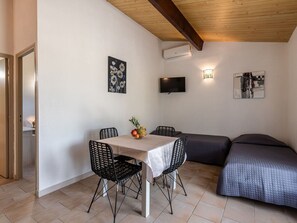 Una habitación pequeña y bien iluminada con una mesa de comedor, sillas, una cama y obras de arte en las paredes.