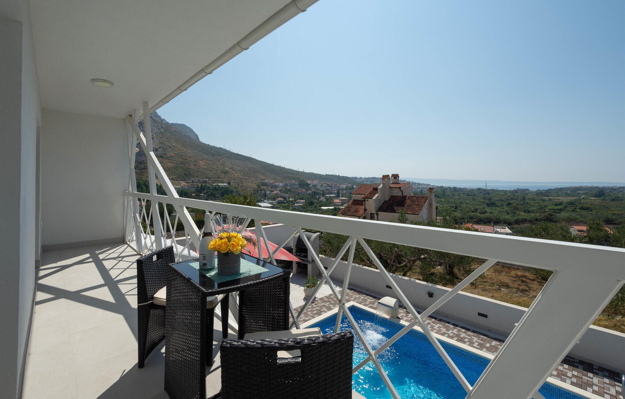 A balcony with a pool, wicker furniture, and a view of a town and mountains.