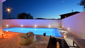 An outdoor swimming pool area with a stone deck, a lounge chair, and a table with drinks and a lantern. - Beautiful home in Pozorac (Pozorac)