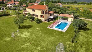 A large house with a swimming pool, surrounded by a well-maintained lawn and a soccer goal.