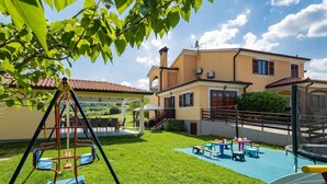 A sunny outdoor area with a swing set, a slide, and a covered seating area with tables and chairs.