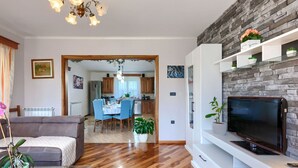 A modern living room with a flat-screen TV, wooden flooring, and a dining area in the background.