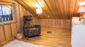A cozy attic room with wooden walls, a floral-patterned chair, a white rug, and a floor lamp.