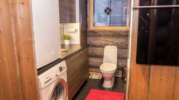 A compact bathroom with a washing machine, toilet, and a small window with blinds.