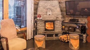 A cozy room with a stone fireplace, a comfortable chair, a television, and a window with blinds.