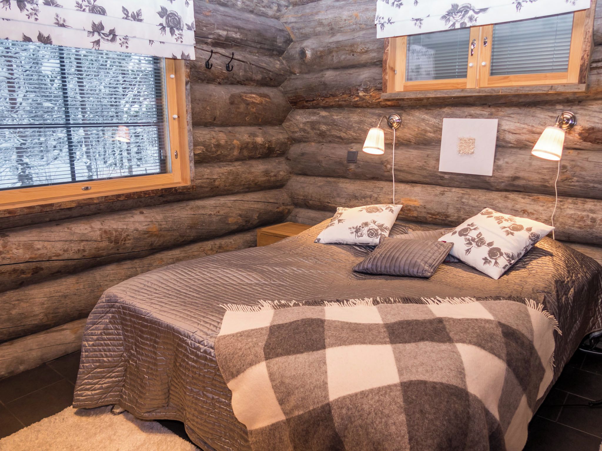 A log cabin bedroom with a bed, two pillows, a window with blinds, and a hanging light fixture.