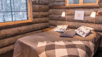 A log cabin bedroom with a bed, two pillows, a window with blinds, and a hanging light fixture.