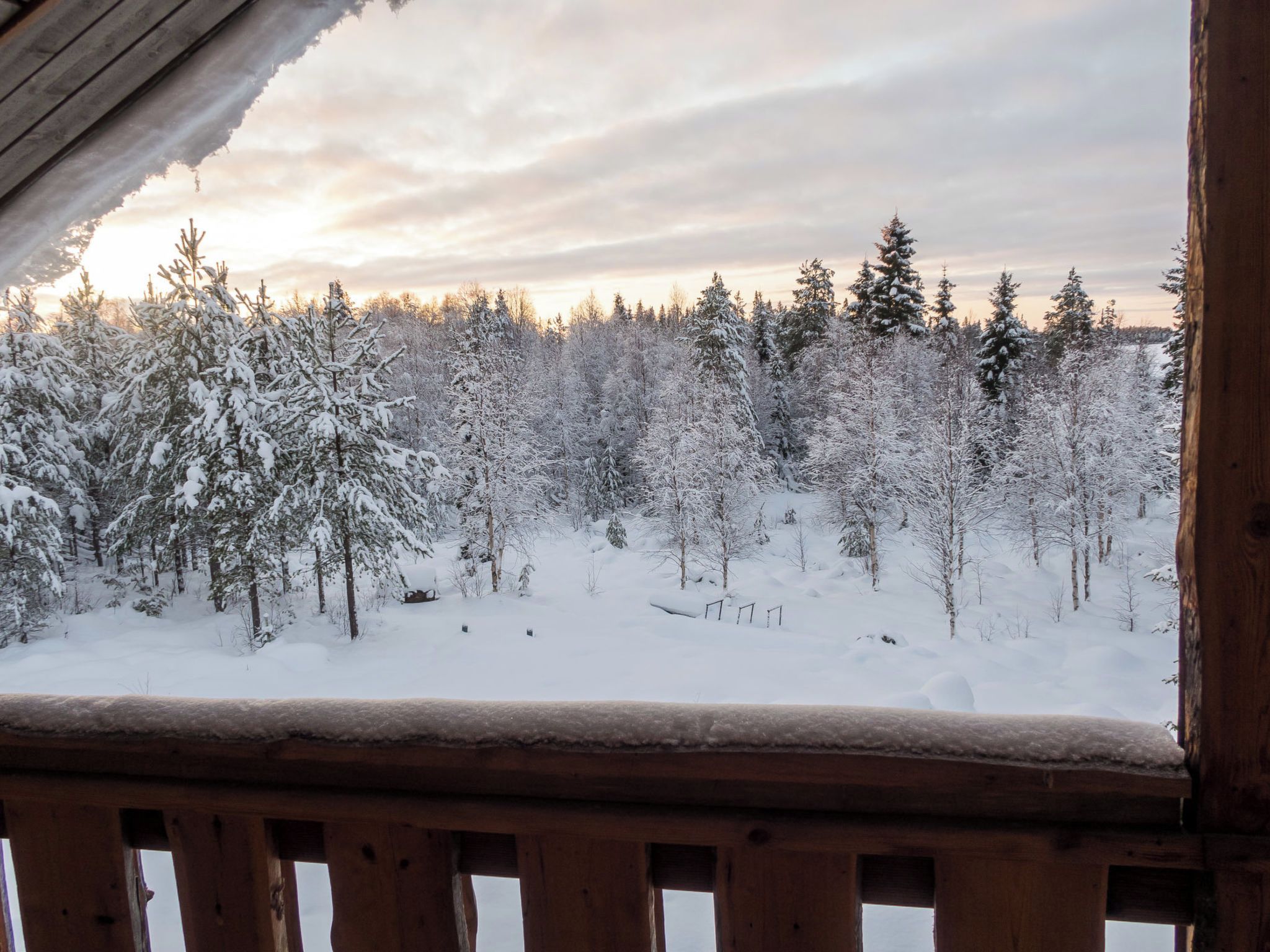 Schneeiger Blick auf einen Wald von einer Holzhütte mit einer Terrasse aus.