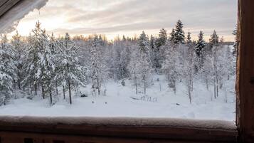 Schneeiger Blick auf einen Wald von einer Holzhütte mit einer Terrasse aus.