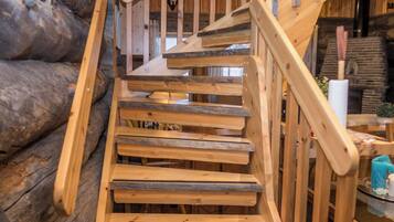 Eine Holztreppe mit Geländer, umgeben von Holzbalken und einem Steinkamin.