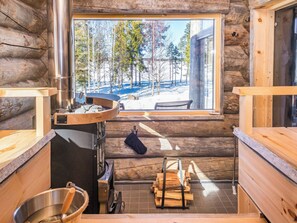 Et interiør af en hytte med store vinduer, en træovn og en sauna bænk.