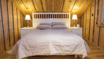 A bedroom with a wooden ceiling, a white bed with a headboard, two bedside tables with lamps, and a fluffy white rug.