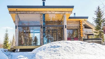 A modern log cabin with a glass facade, wooden logs on the exterior, and a snow-covered ground.