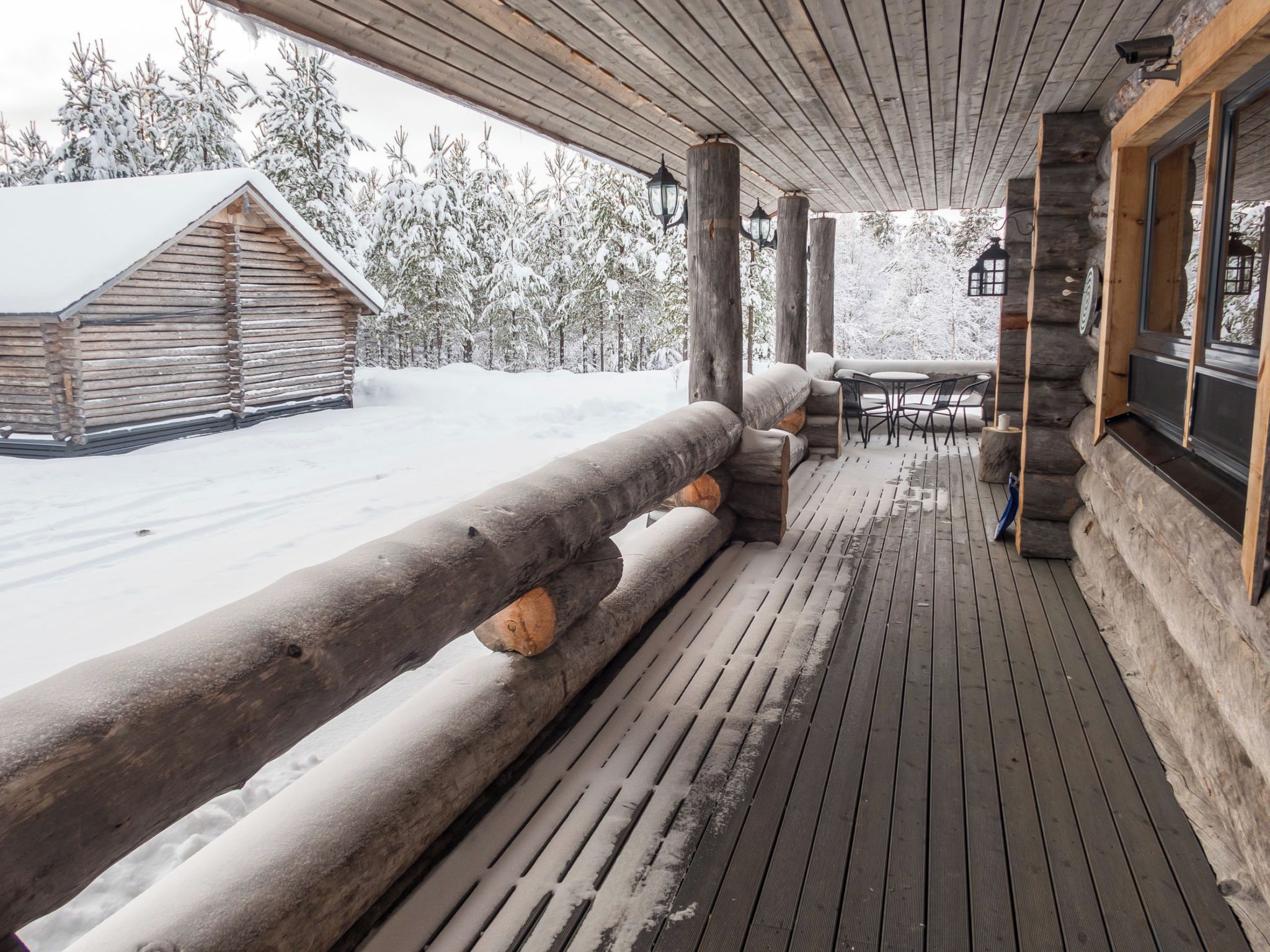 A log cabin with a wooden deck, outdoor seating, and snow-covered trees.