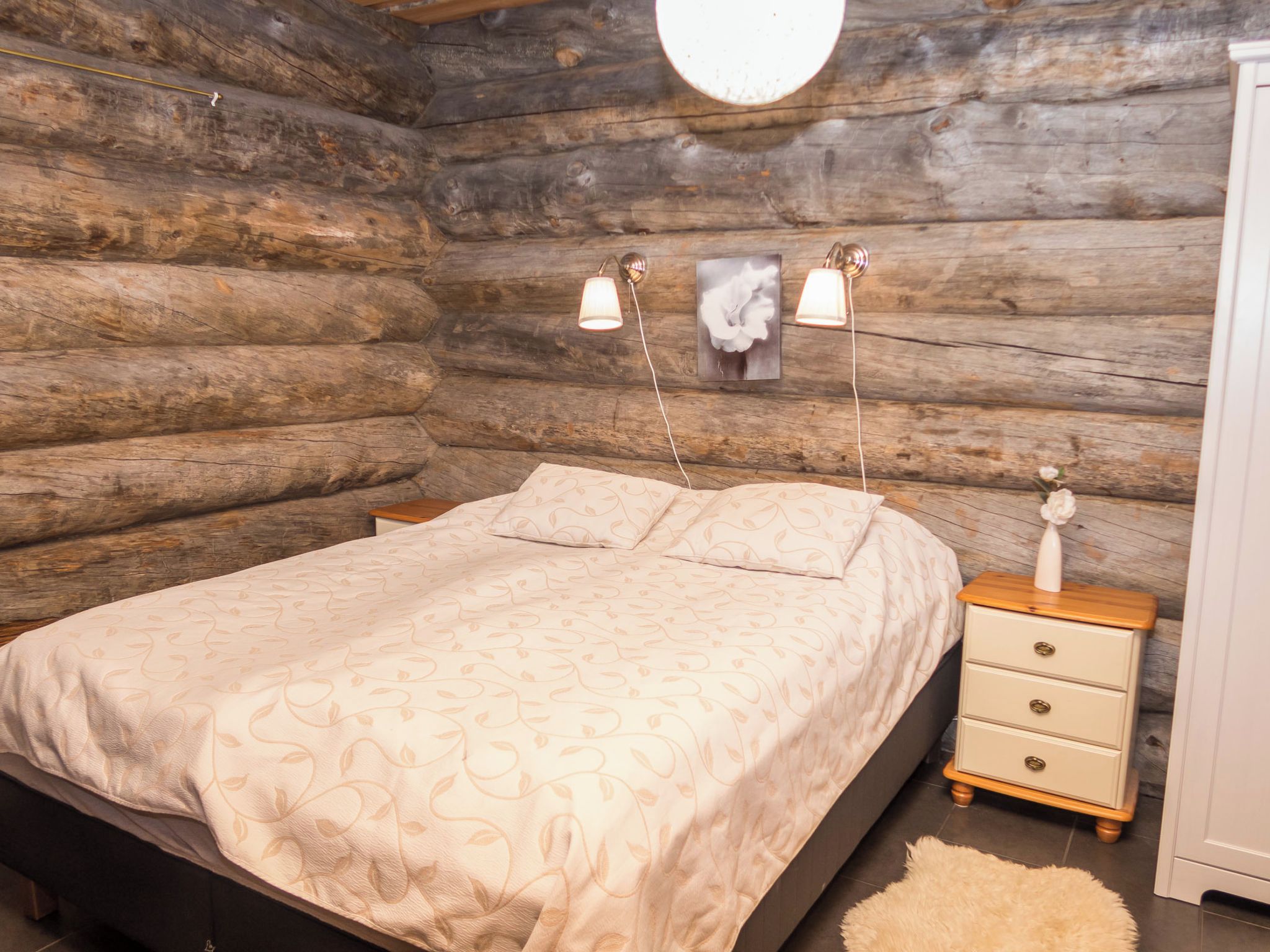 Un dormitorio de cabaña de troncos con cama, lámparas de noche, cómoda y una lámpara de pared.