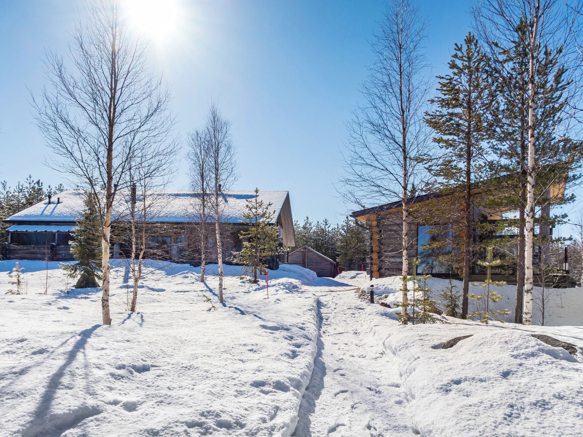 A snow-covered landscape with a building featuring a sloped roof and a wooden cabin.