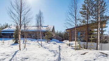 A snow-covered landscape with a building featuring a sloped roof and a wooden cabin.