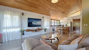 A modern living room with a large sofa, wooden ceiling, and a dining area with a table and chairs.