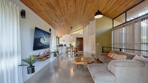 A modern living room with a wooden ceiling, a large painting, a sofa, and a dining area.