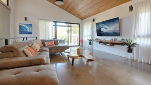 A spacious living area with a wooden ceiling, a large sofa set, a coffee table, and a mounted painting.