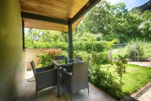 Eine Terrasse im Freien mit Tisch und Stühlen, umgeben von Grünpflanzen und einem Zaun.