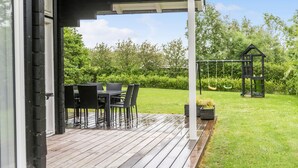 Een overdekt terras met een tafel, stoelen, een schommel en een tuin.