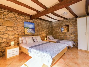 A bedroom with two beds, stone walls, wooden beams, and a painting of a beach scene.