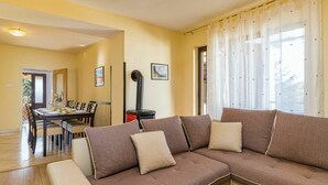 A living room with a brown sofa, a dining table with chairs, and a black stove. - Beautiful private villa for 8 guests with A/C, internet, private pool, TV, terrace and pets allo... (Buzet)