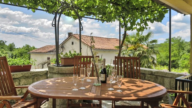A round wooden table with four chairs, a bottle of champagne, and several glasses on a patio with a view of a house and greenery. - Beautiful private villa for 8 guests with A/C, internet, private pool, TV, terrace and pets allo... (Buzet)