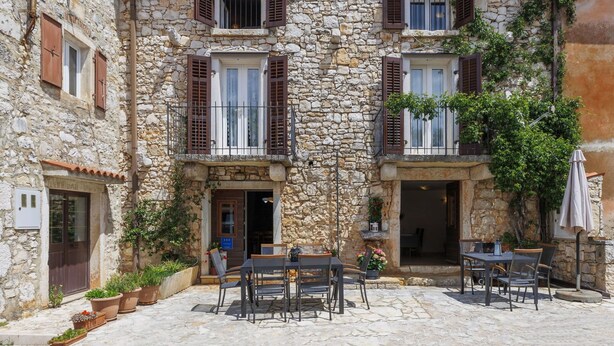 A stone building with multiple windows and shutters, outdoor seating area with tables and chairs, and potted plants. - Wonderful  villa for 8 people with A/C, WIFI, TV, terrace and pets allowed (Umag)