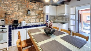 A rustic kitchen with stone walls, white cabinets, and a dining area with a table set for four. - Wonderful  villa for 8 people with A/C, WIFI, TV, terrace and pets allowed (Umag)
