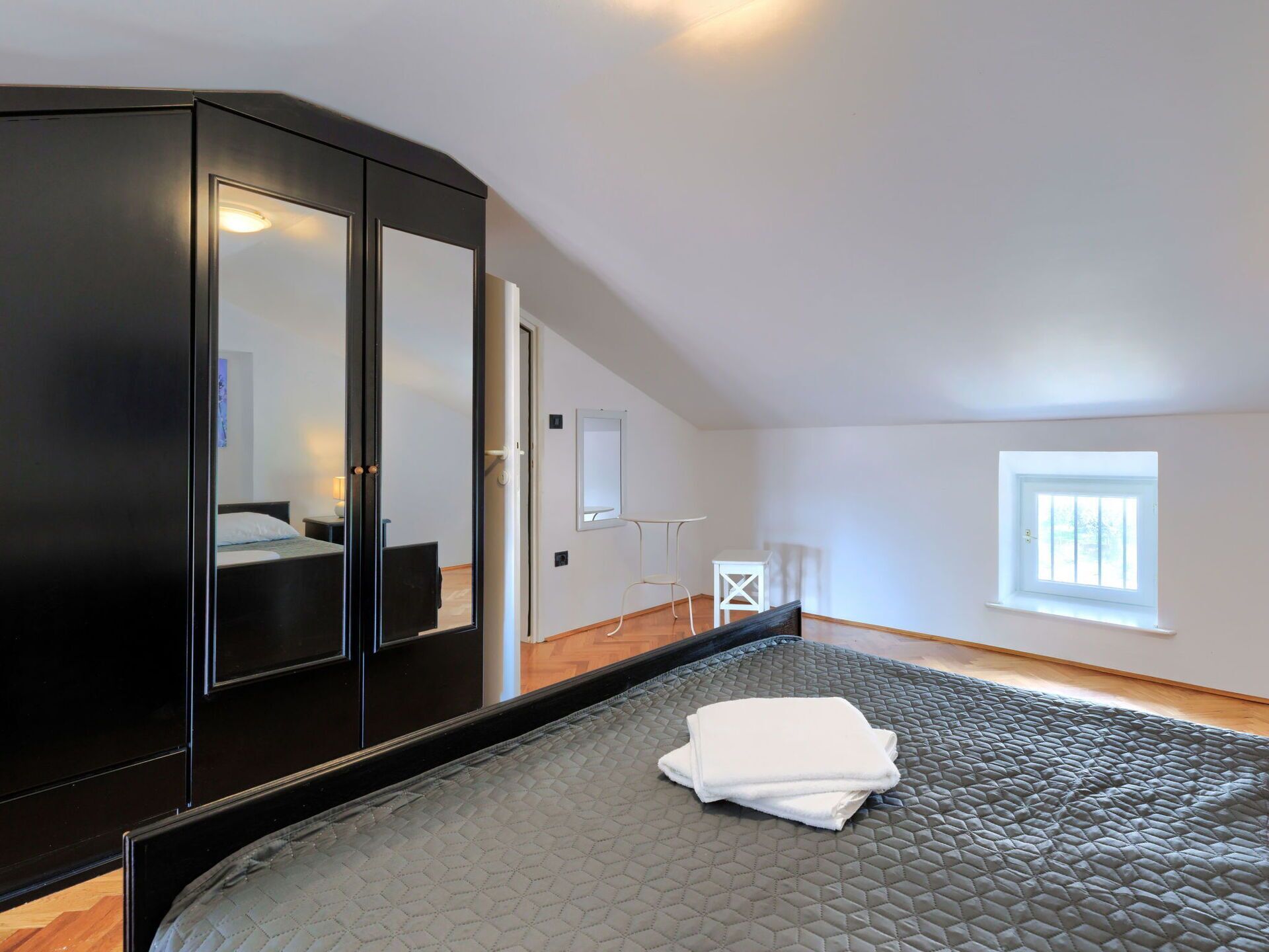 A bedroom with a large bed, a wardrobe, a small table, and a window.