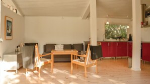 Amplia sala de estar con piso de madera, un conjunto de sofás, una mesa de comedor y una cocina con gabinetes rojos.