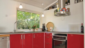 Una cocina moderna con armarios rojos, horno empotrado, ventana con vista a zonas verdes y diversos utensilios de cocina sobre la encimera.