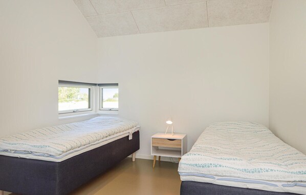 A bedroom with two beds, a nightstand, and a window.