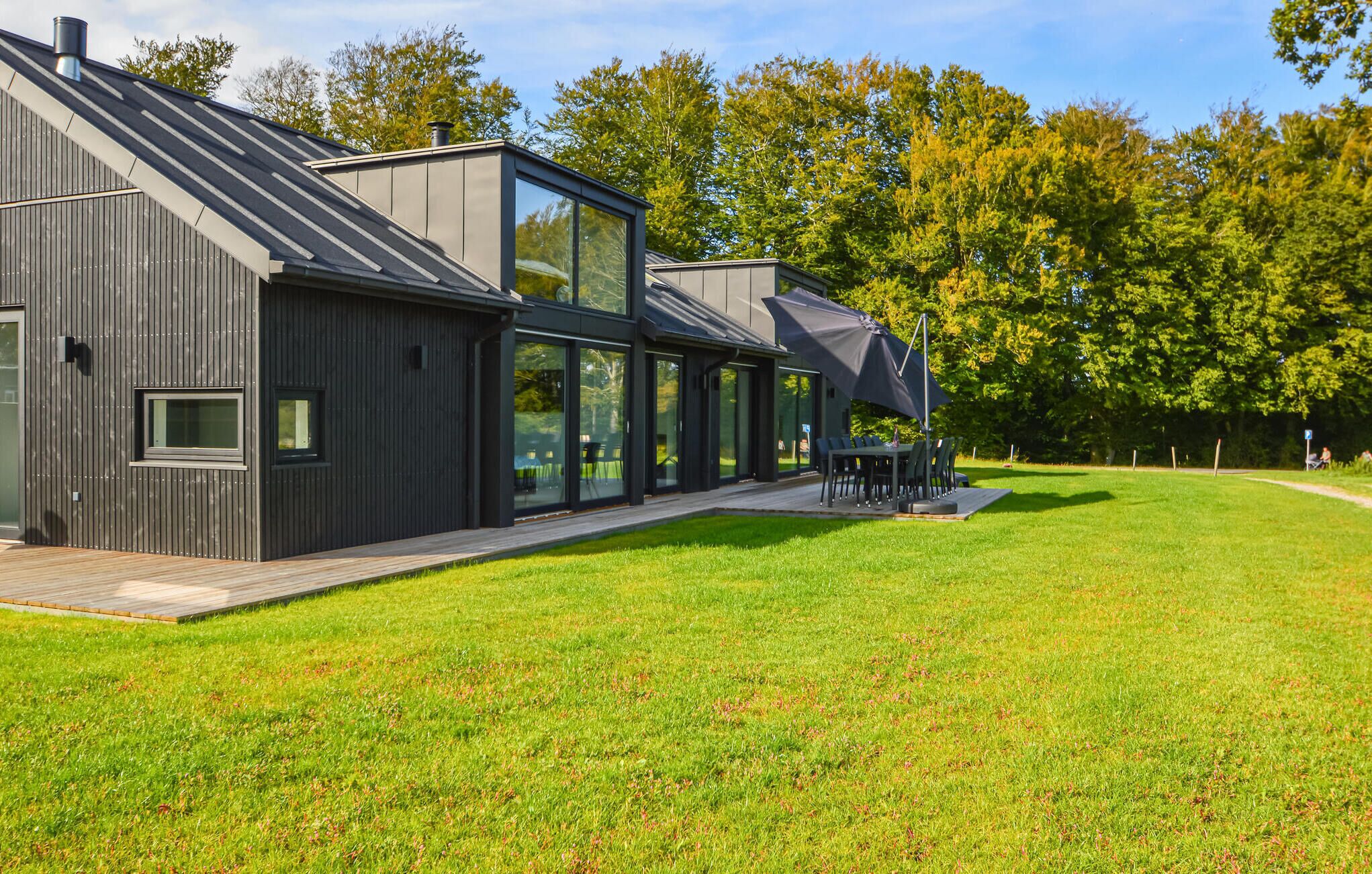A modern building with a large glass facade, a wooden deck, and a grassy lawn.