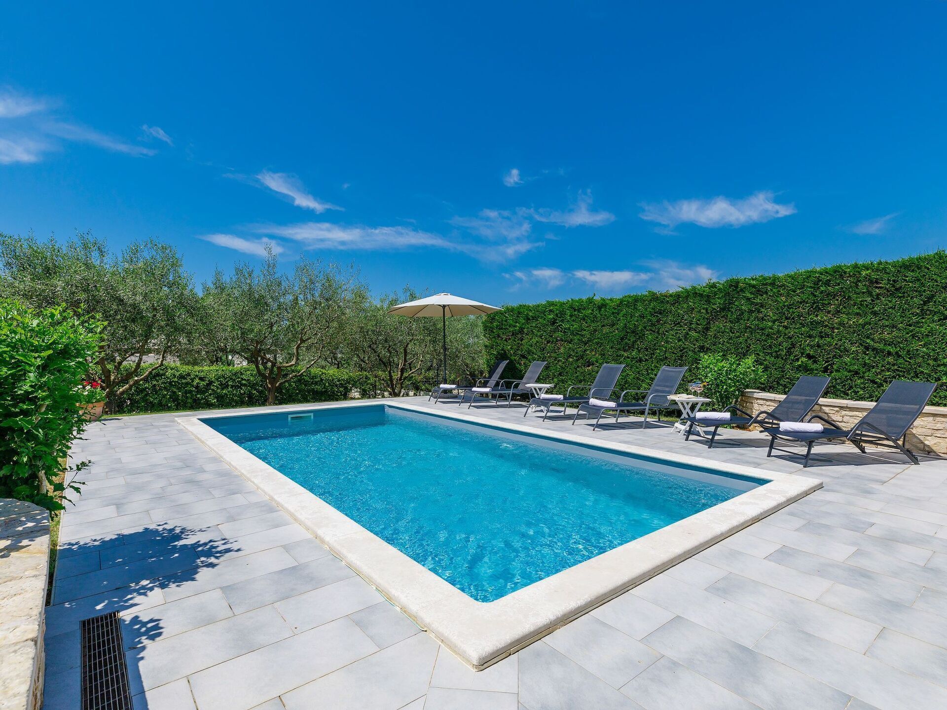 Una piscina rectangular amb terrassa enrajolada, envoltada de gandules i una tanca.