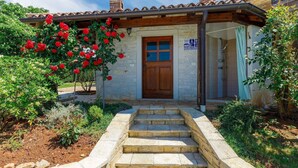 A stone house with a wooden door, a small porch, and a staircase leading to the entrance.