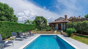 A rectangular swimming pool with lounge chairs and a stone pathway leading to a house with a tiled roof.