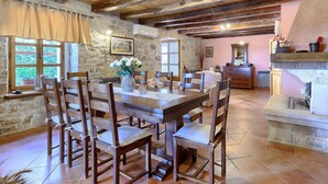 A rustic dining area with a stone wall, wooden beams, and a large table with chairs.