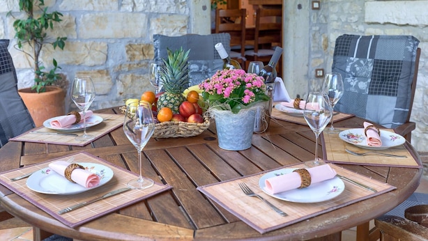 A wooden table set for four with plates, cutlery, and wine glasses. There are potted plants and a fruit basket on the table.