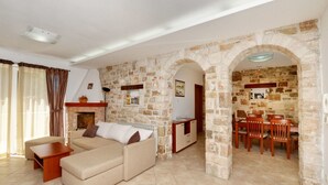 A living room with a sofa, a dining table with chairs, and stone walls. - Beautiful private villa for 7 guests with A/C, WIFI, TV, terrace and pets allowed (Umag)