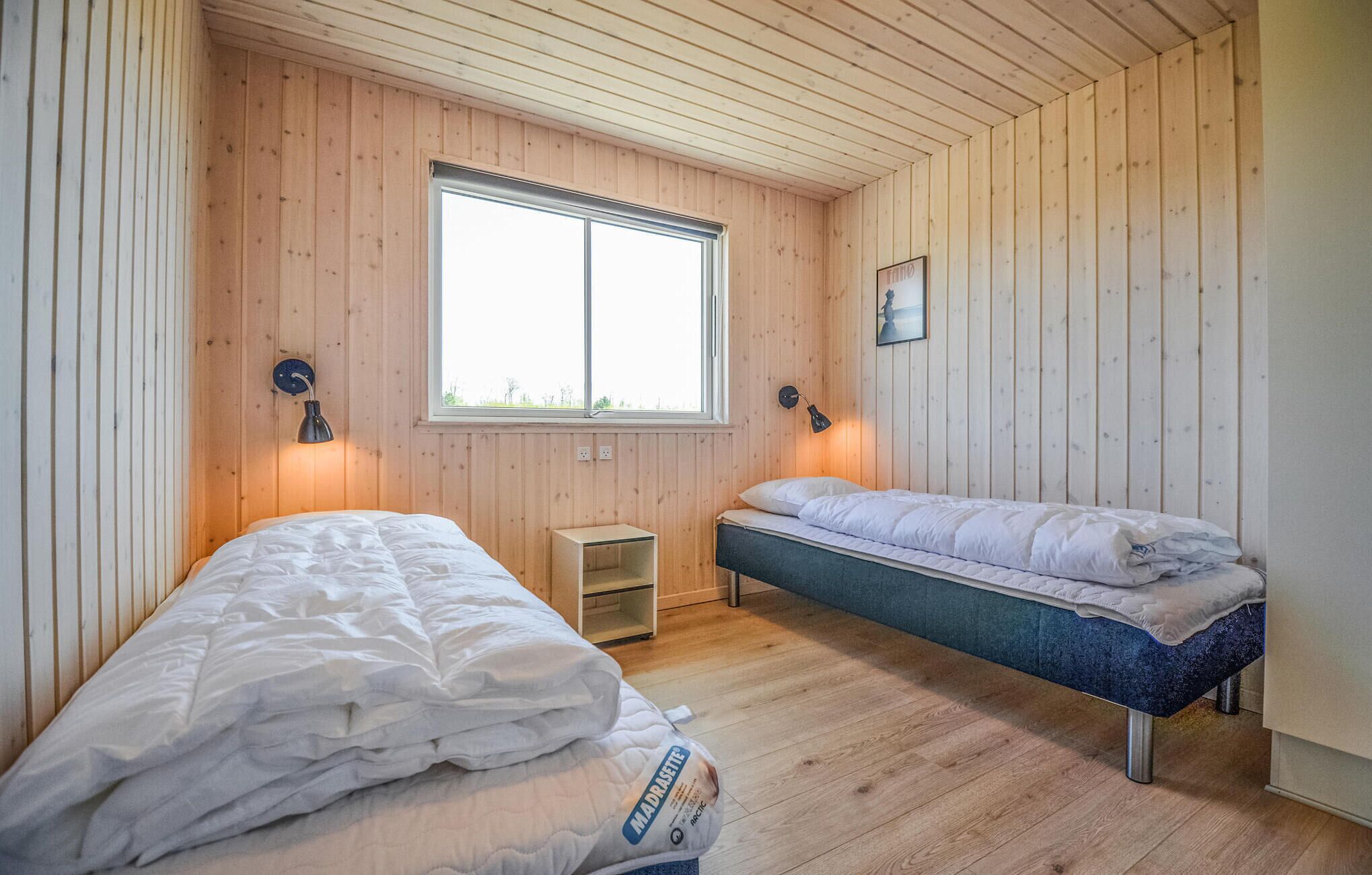Une pièce aux murs en bois, avec deux lits, une fenêtre et une petite table.