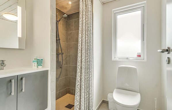 Un baño con ducha, inodoro y espejo.
