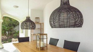 A dining area with a wooden table, two black woven pendant lights, and a view of greenery through an archway. - Beautiful home in Trullent (Trullent)