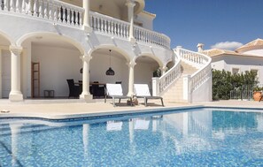 Zona de piscina amb un edifici blanc, una escala i seients de relax.