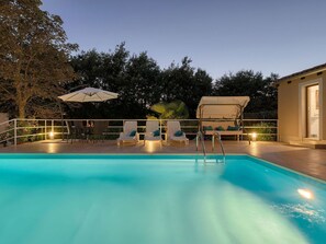 A swimming pool with lounge chairs and umbrellas, surrounded by trees and a building.
