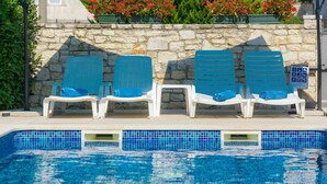 Un espace aménagé au bord de la piscine, comprenant quatre chaises longues bleues, un mur en pierre et un panneau indiquant la présence d’une piscine.
